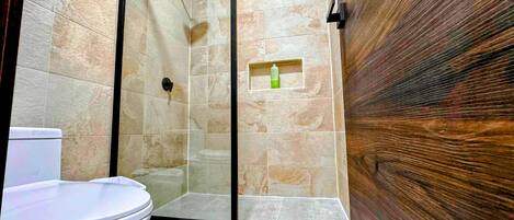 A bathroom with a shower, toilet, and a small shelf with a bottle.