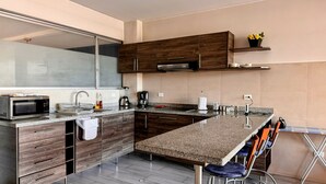 A modern kitchen with a granite countertop, wooden cabinets, a built-in microwave, and a coffee maker. - Edificio Tofino (Quito)