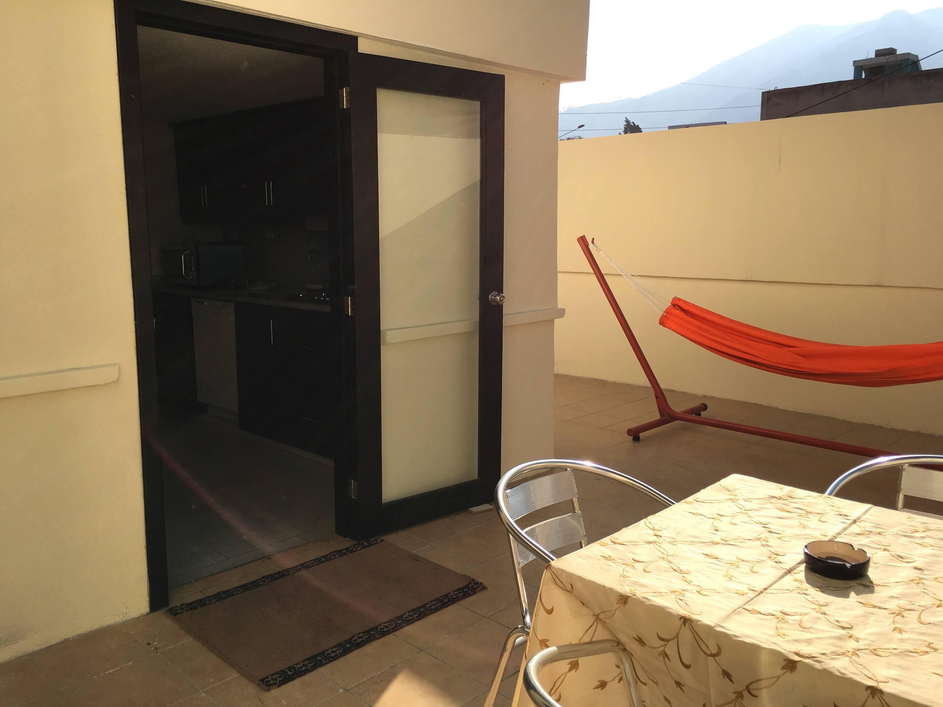 A balcony with a table, chairs, a hammock, and a sliding door leading to a kitchen area.