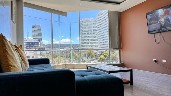 Una sala de estar moderna con un amplio ventanal que ofrece vistas a la ciudad, un sofá cómodo y un televisor de pantalla plana en la pared.