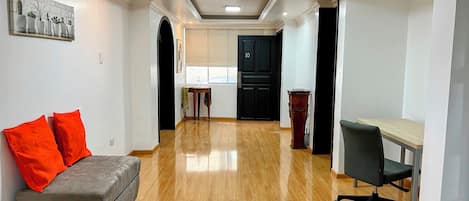 A hallway with a grey sofa, a desk, and a black chair. There is a black door with the number 10 on it, and a small table with a water bottle.