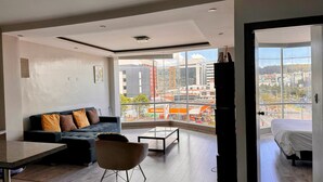 A modern living room with a sofa, a coffee table, and a view of a cityscape through large windows. - Edificio Tofino (Quito)
