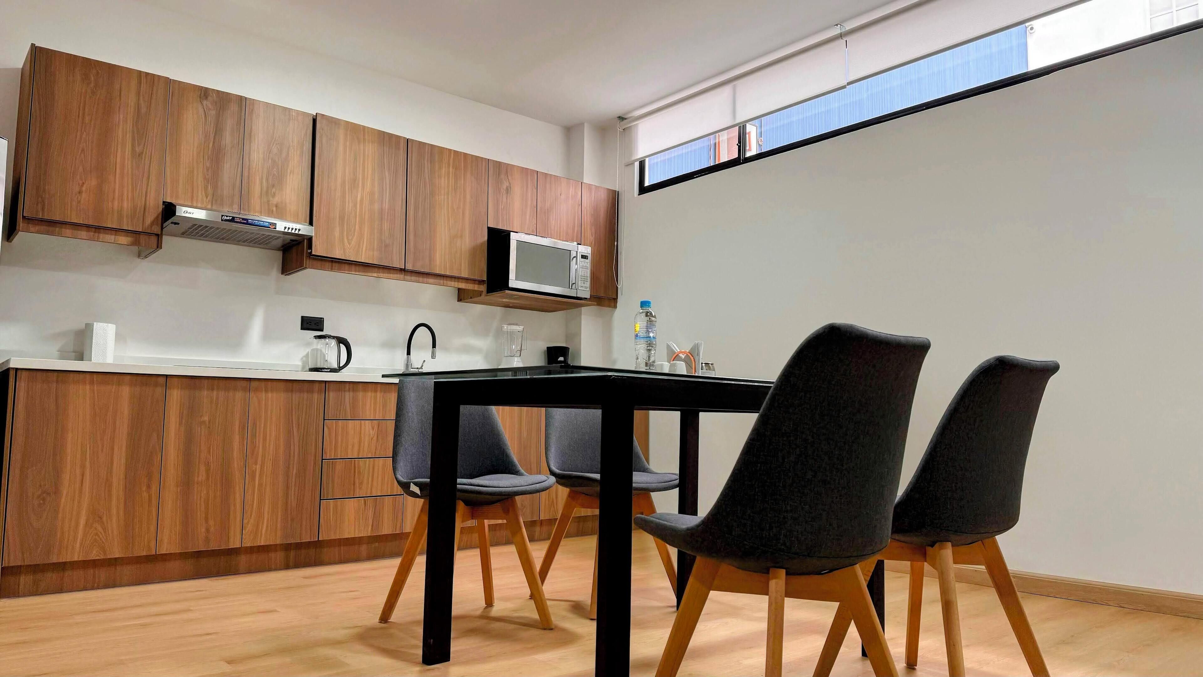 A modern kitchen with wooden cabinets, a microwave, and a dining area with a black table and four chairs.