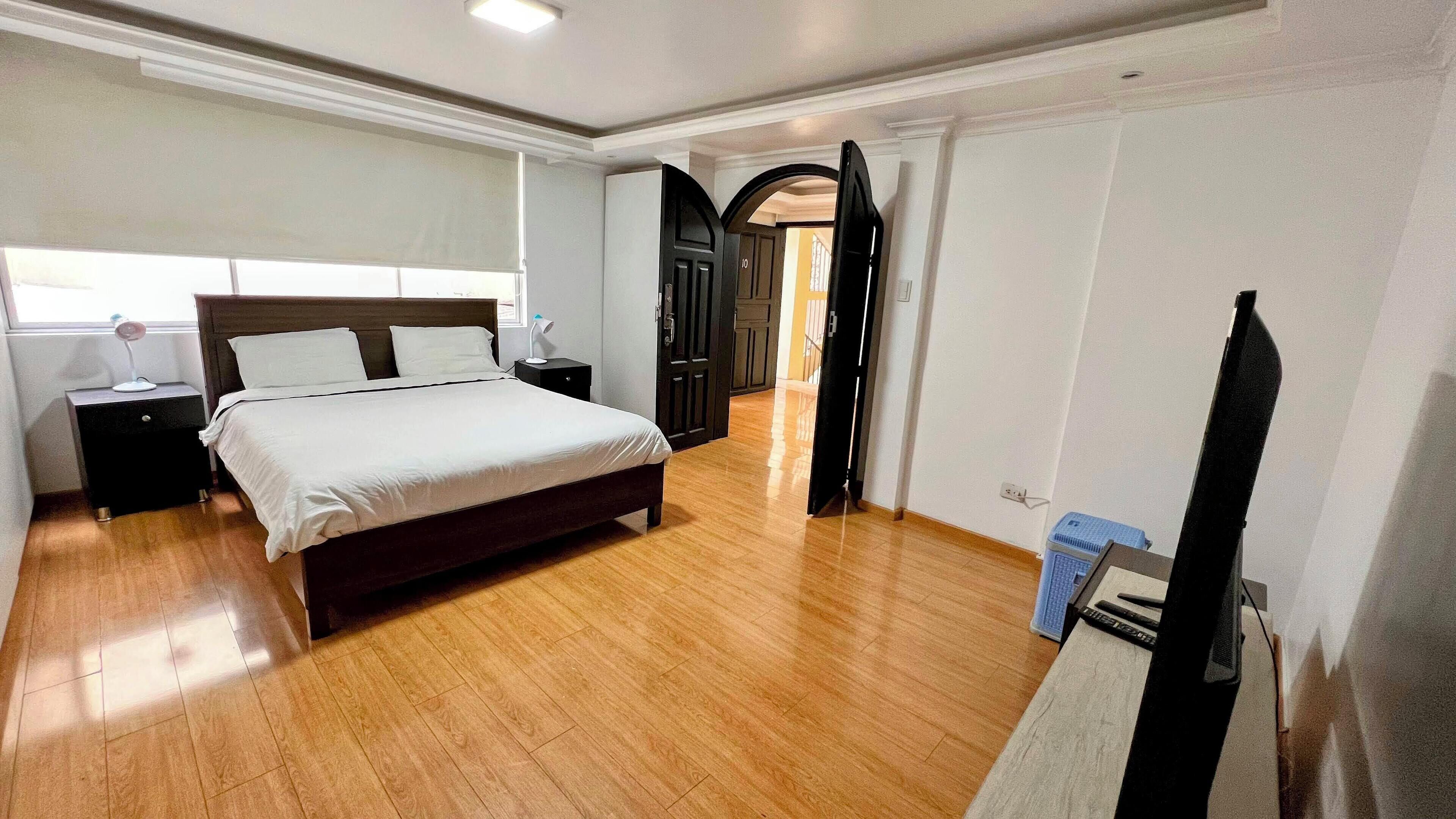 A bedroom with a bed, bedside tables, a desk, and a TV.