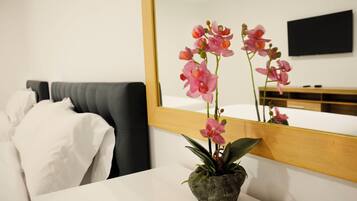 Habitación de hotel con cama, mesita de noche blanca con orquídea en maceta y un espejo grande que refleja la habitación.