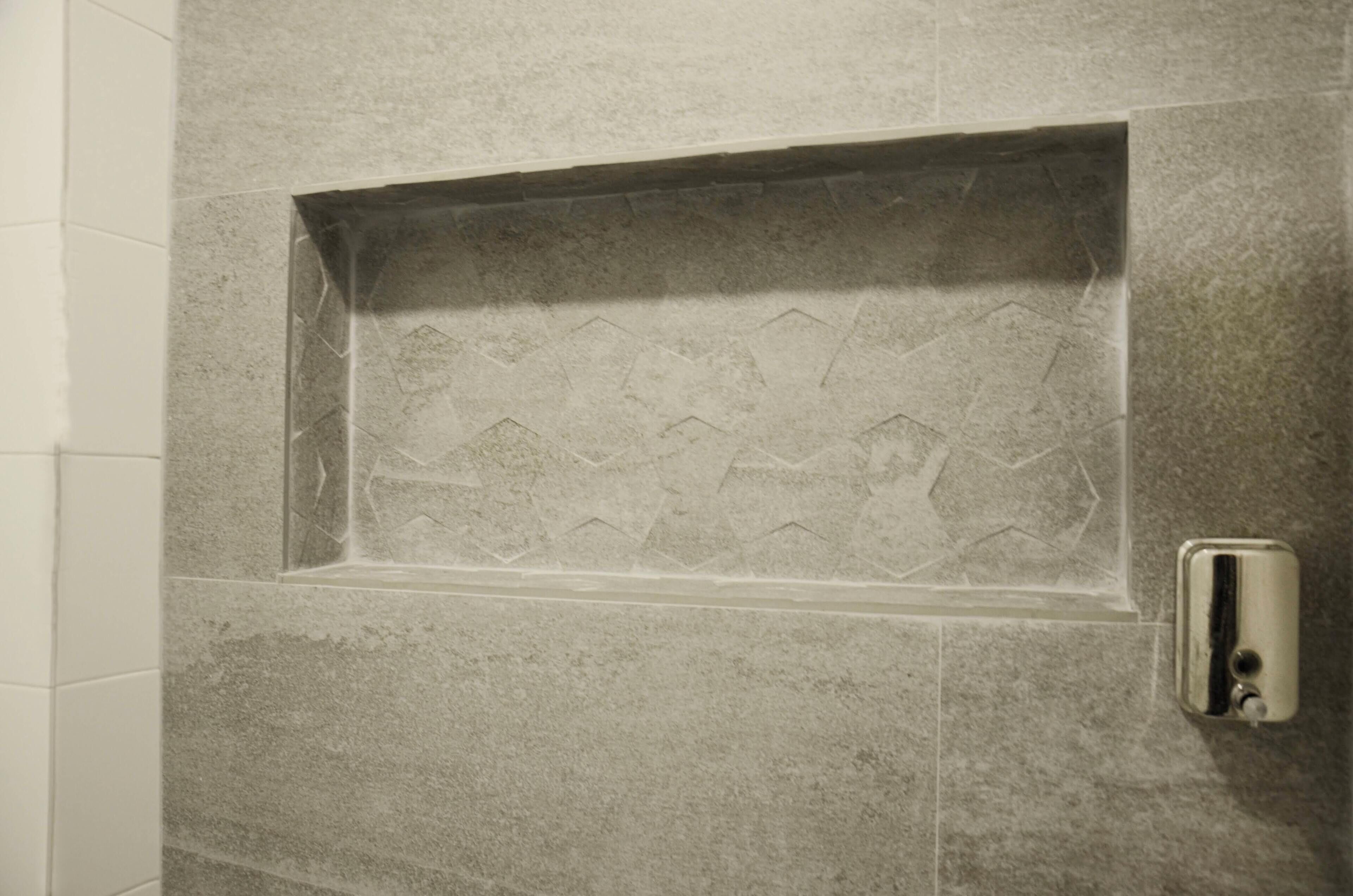Ein Badezimmer mit einem rechteckigen Waschbecken, das in eine strukturierte Wand eingelassen ist, einem Seifenspender und einem gefliesten Boden.