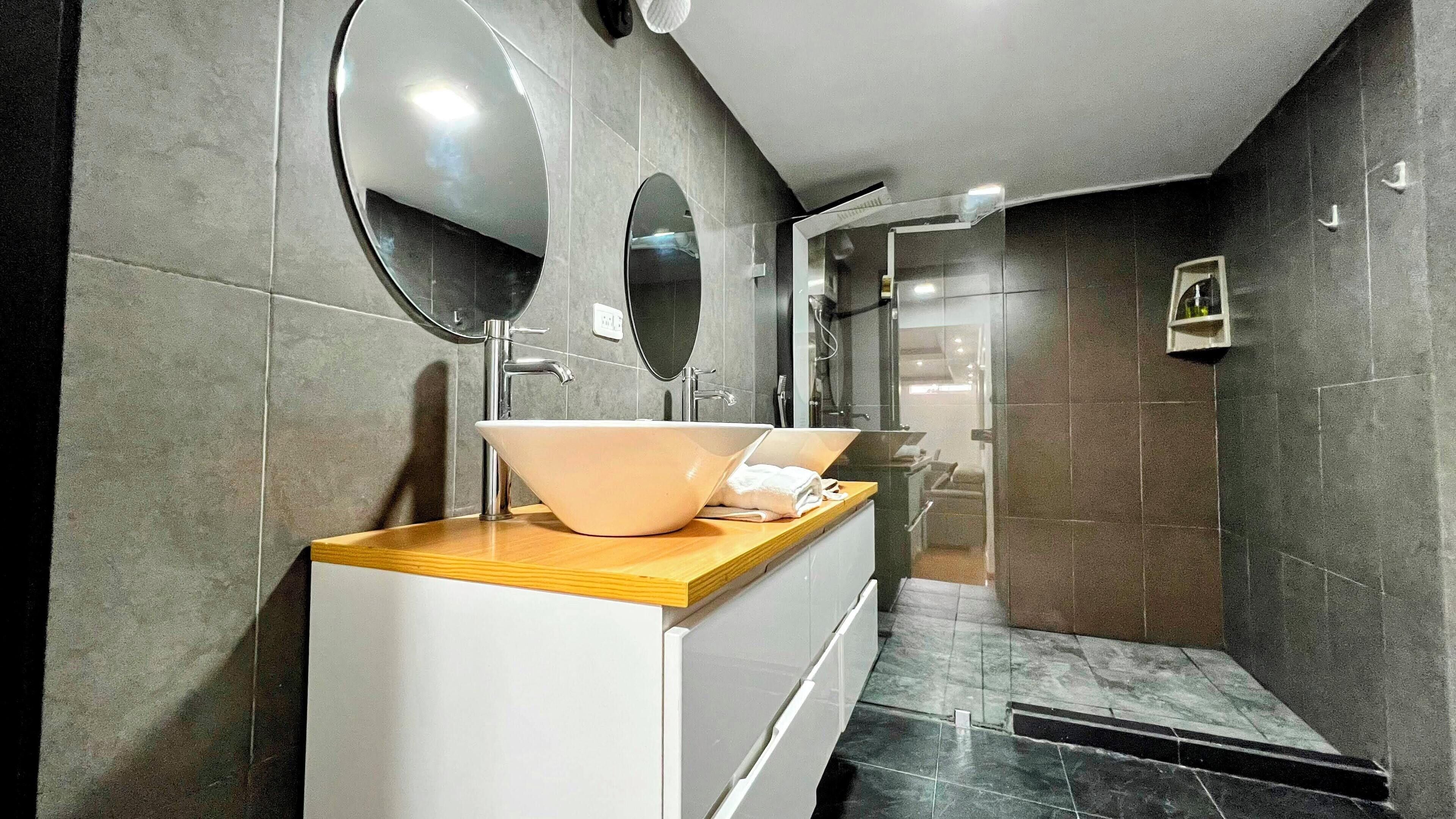 A modern bathroom with two sinks, a mirror, and a shower area.