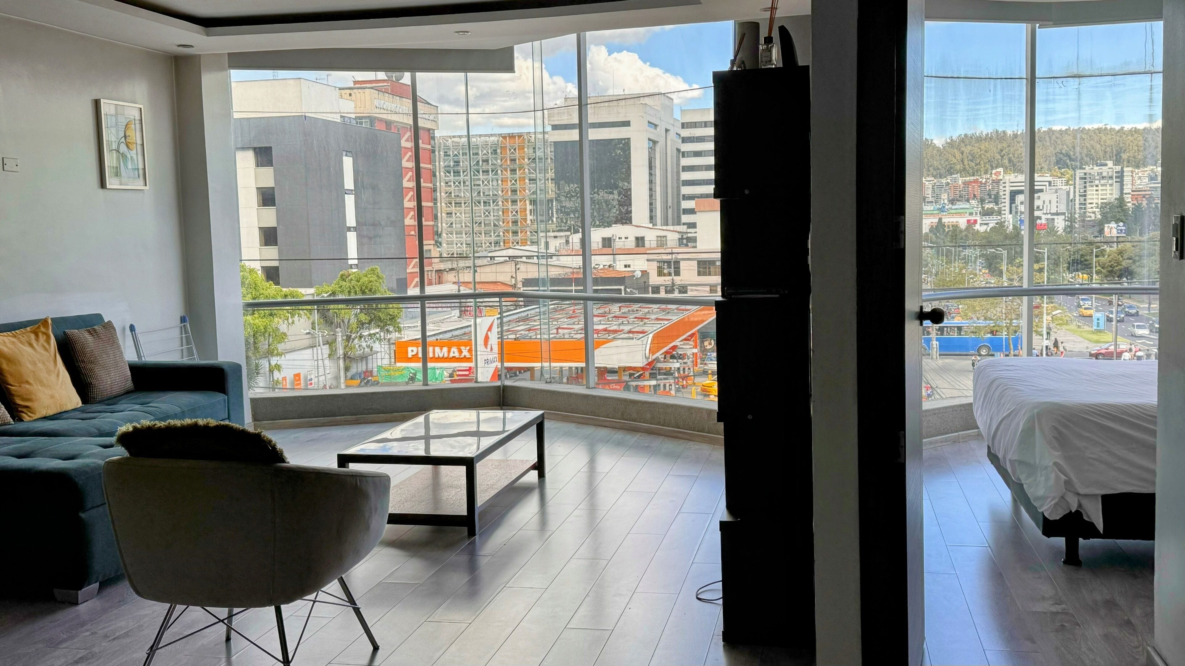 A modern living room with a large window, a sofa, a chair, and a bed.