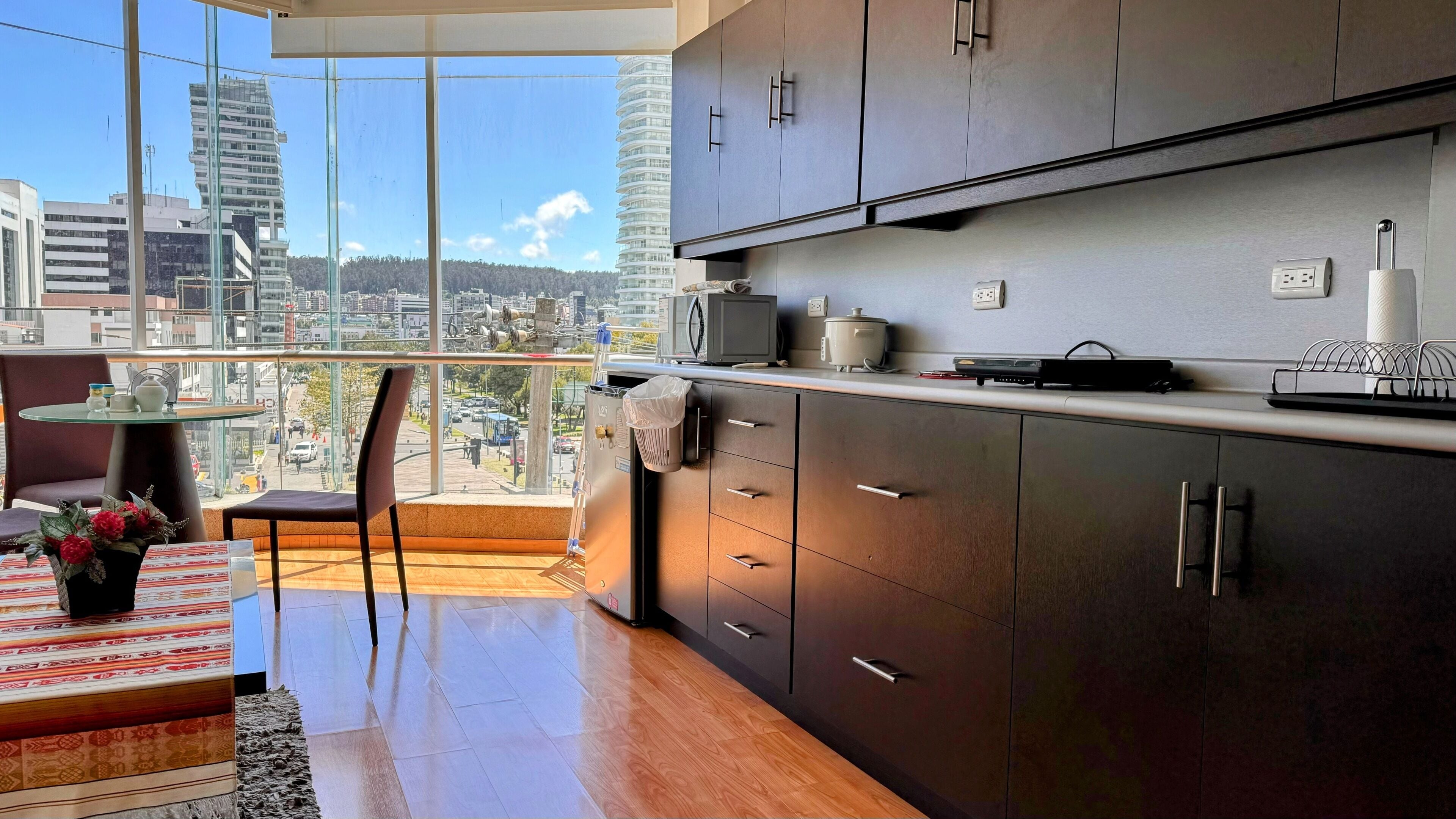 Una cucina moderna con mobili scuri, un tavolo con piano in vetro e vista sulla città.