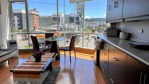 A modern kitchen with a large window, a dining area with a table and chairs, and a view of the cityscape. - Edificio Tofino (Quito)