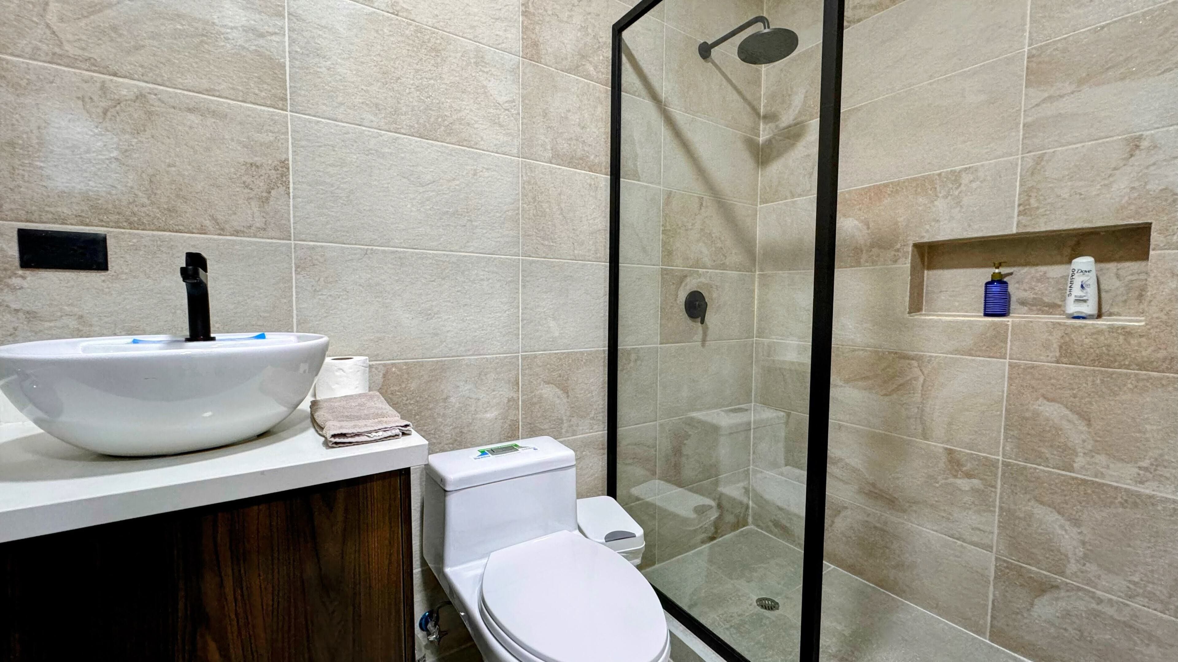A modern bathroom with a white sink, toilet, and glass-enclosed shower.