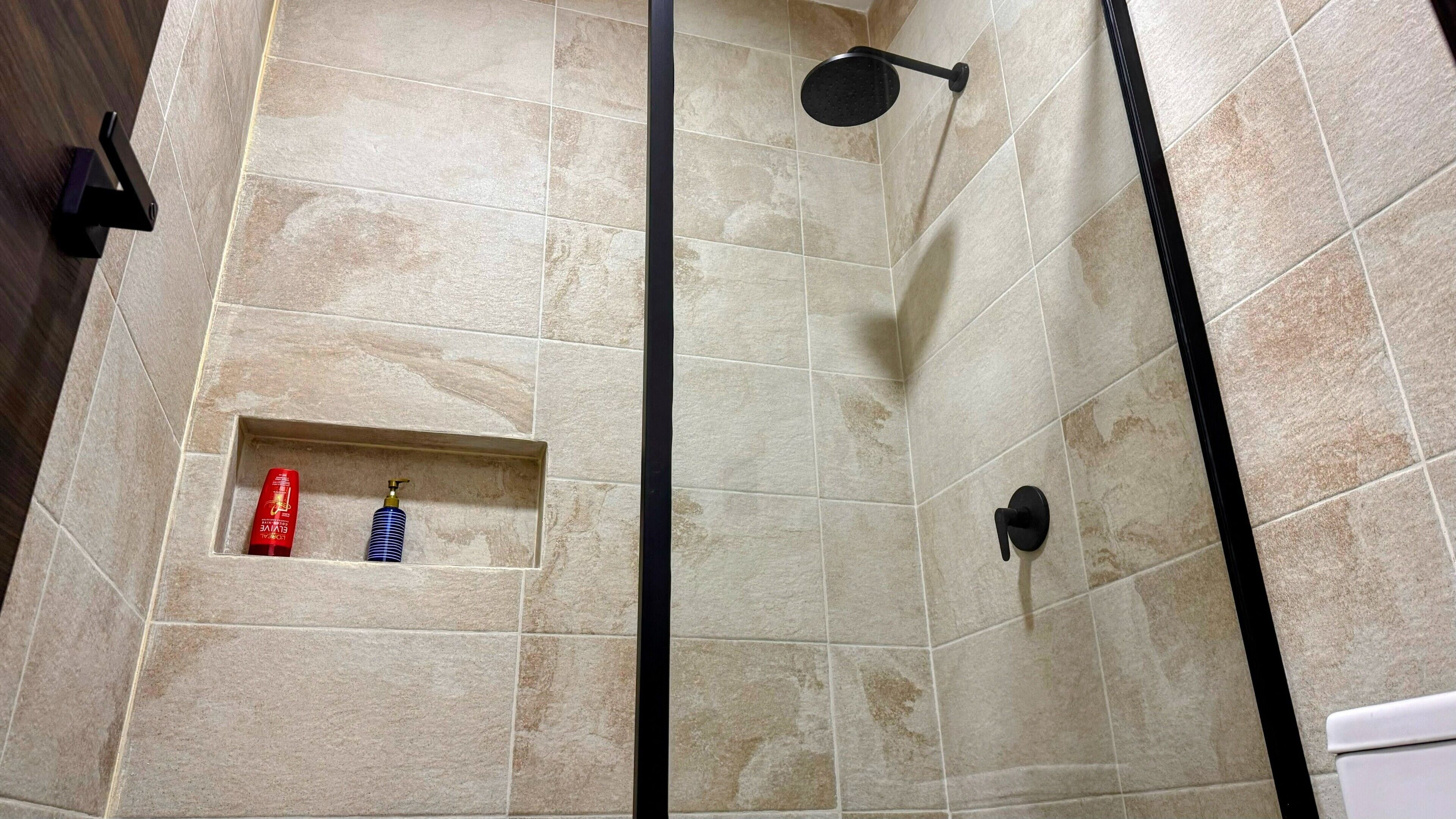 A shower area with beige tiles and a black showerhead.