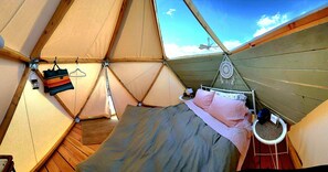 Una tienda acogedora con cama, un bolso colgado, un farol y un atrapasueños.