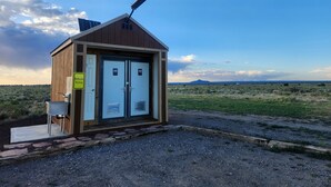 Un piccolo edificio a un piano con due porte, un pannello solare sul tetto e un cartello che indica servizi igienici e parcheggio.