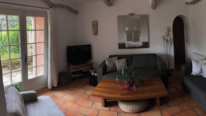 Ein Wohnzimmer mit einer Couch, einem Couchtisch mit Pflanze, einem Fernseher und einem Fenster mit Vorhängen.