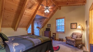 A bedroom with a wooden ceiling, a bed with a quilt, a chair, a desk, and a window with a view. - Bear Creek (Sugar Grove)