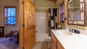 A bathroom with a wooden door, a bathtub, a toilet, and a sink with a mirror. - Bear Creek (Sugar Grove)