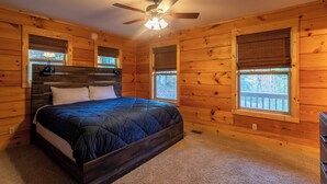 A wooden cabin bedroom with a bed, ceiling fan, and windows. - Firefly Cabin (Banner Elk)