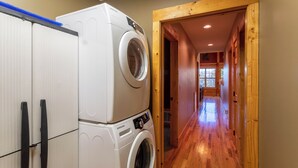 A laundry area with stacked washing machines and dryers, wooden flooring, and a hallway leading to another room. - Firefly Cabin (Banner Elk)