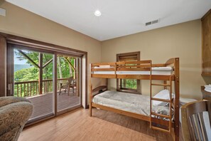 A room with a bunk bed, a chair, a window with a view of greenery, and a door leading to an outdoor deck. - Apple of my Eye (Banner Elk)