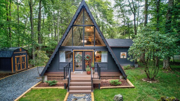 Een moderne, driehoekige cabin met een groot glazen front, omgeven door een bos.