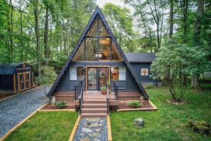 Een moderne, driehoekige cabin met een groot glazen front, omgeven door een bos.