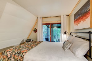 Een slaapkamer met een bed, nachtkastje, raam met gordijnen, een schilderij en uitzicht op bomen.