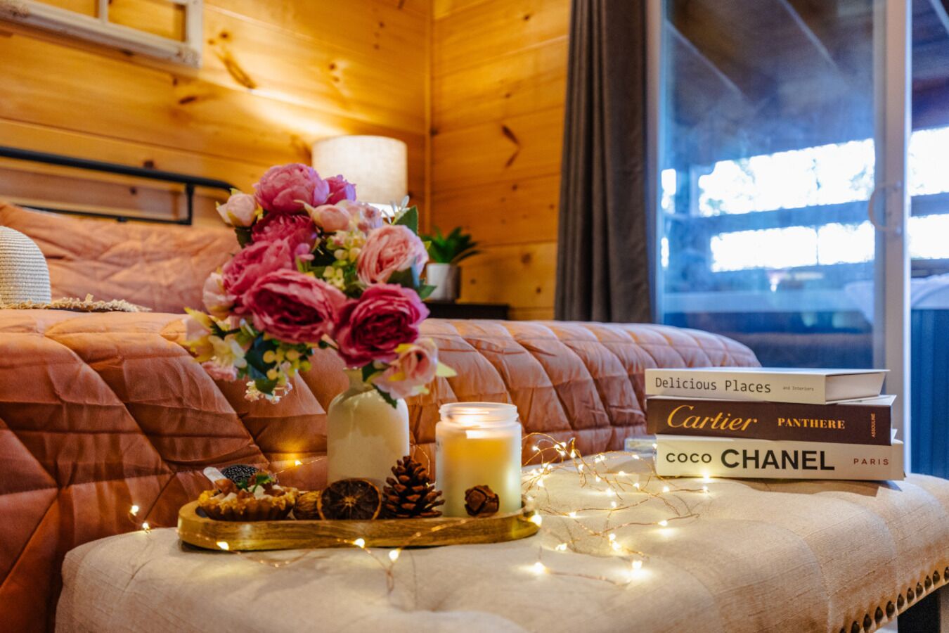 A cozy room with a bed, a vase of flowers, a candle, and a stack of books.