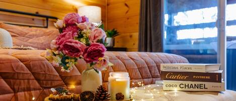 A cozy room with a bed, a vase of flowers, a candle, and a stack of books.