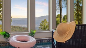 Un espace piscine offrant une vue sur les montagnes et les arbres, grâce à de grandes fenêtres.