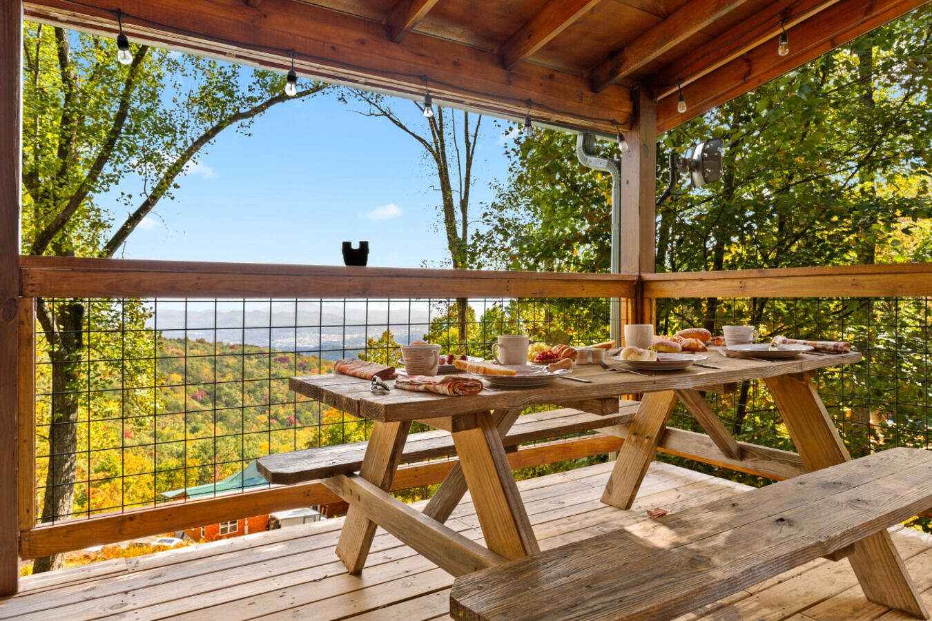 A wooden deck with a picnic table set up, overlooking a scenic landscape with trees and a distant view.