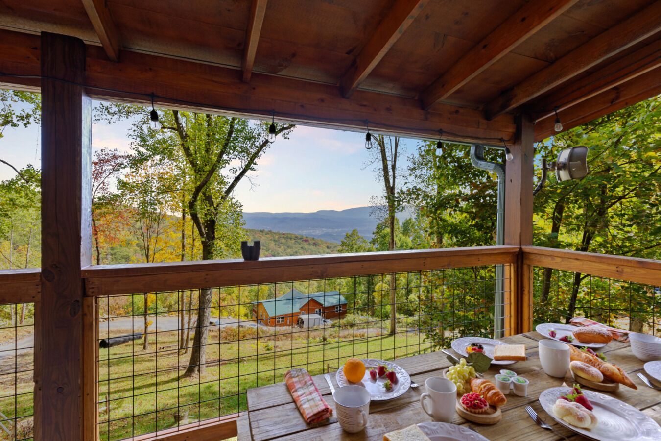 Eine Holzterrasse mit Frühstückstisch, mit Blick auf eine reizvolle Landschaft aus Bäumen und Bergen.
