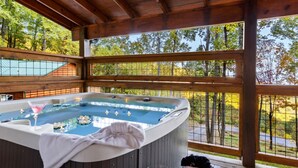Un bain à remous avec une serviette à proximité, entouré d’une terrasse en bois et offrant une vue sur les arbres.