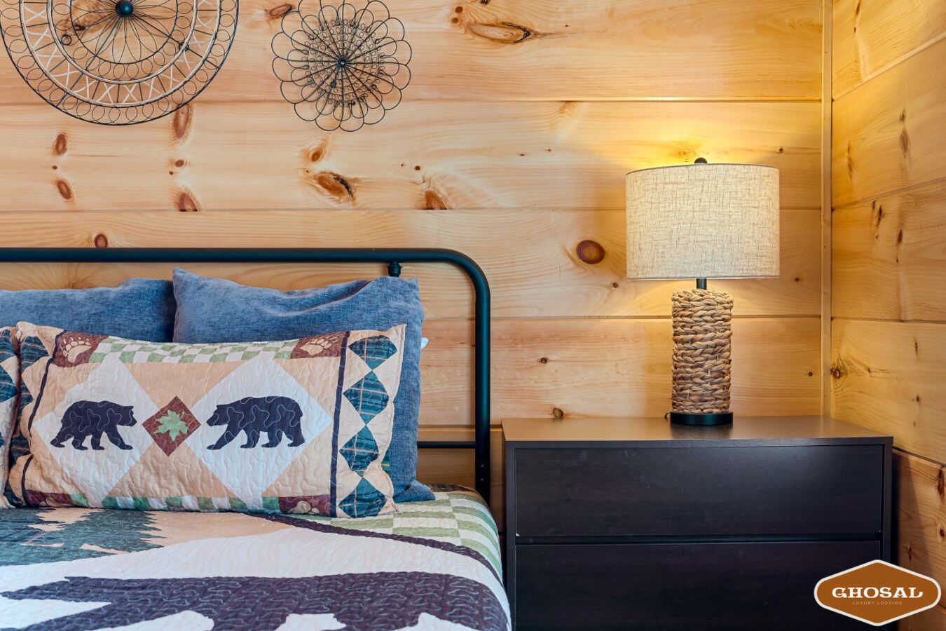 Dormitorio de cabaña de madera con cama, almohadas, mesita de noche, lámpara y decoración en la pared.