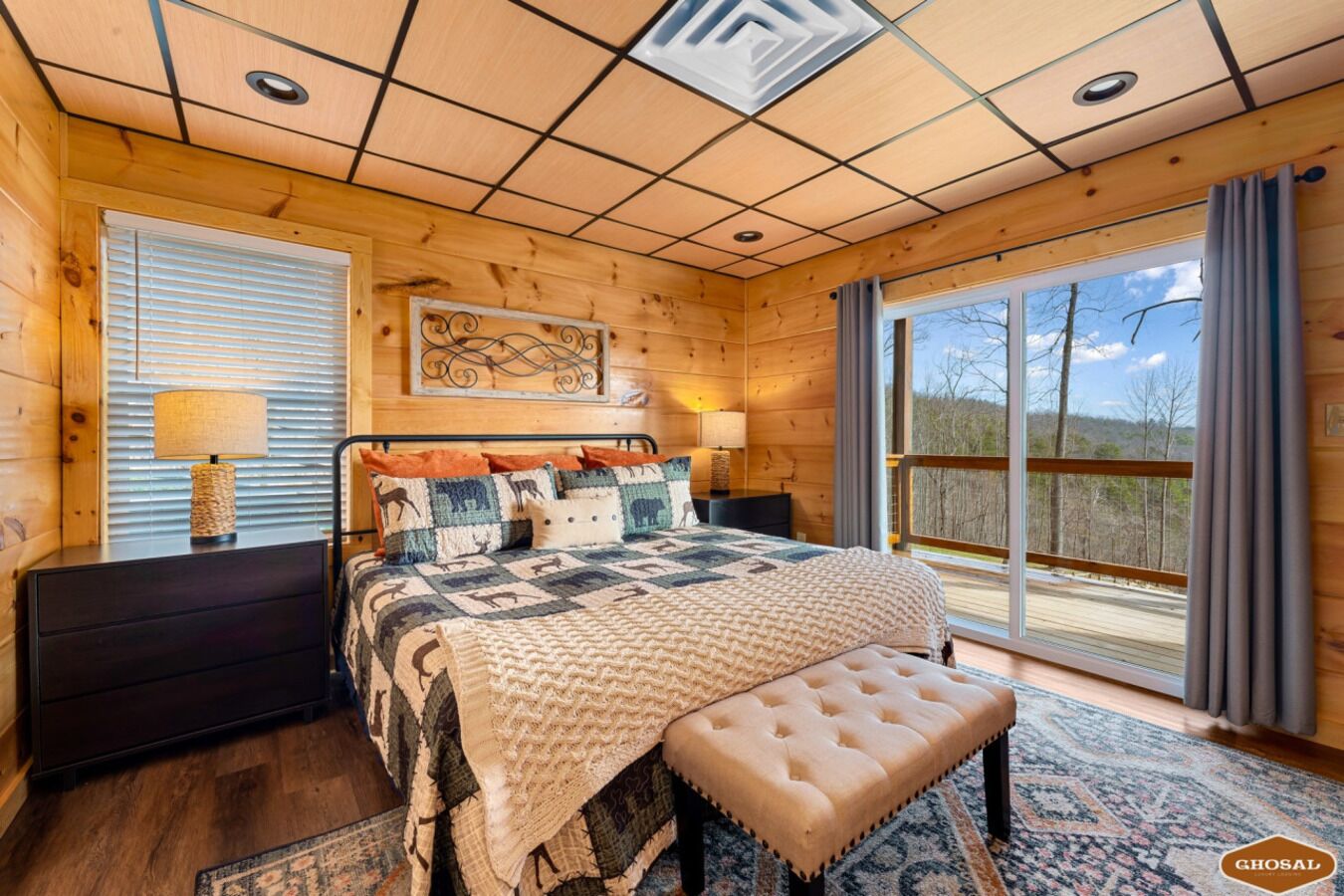 Een gezellige slaapkamer met een groot bed, een bankje, een nachtkastje, een lamp en uitzicht op het groen.