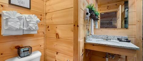A wooden cabin-style bathroom with a toilet, a sink with a mirror, and a sign that says "TAKE A SEAT".
