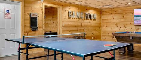 A game room with a ping pong table, pool table, and a sign indicating it is a game room.
