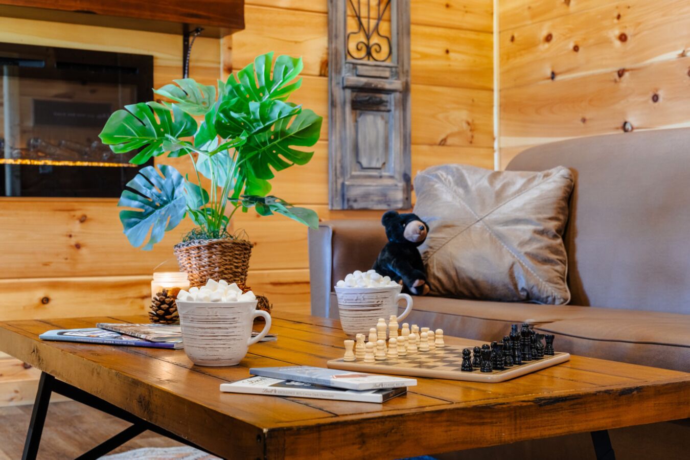 Ein gemütliches Wohnzimmer mit einem Holztisch, einer Topfpflanze, einem Teddybären und einem Schachbrett.