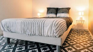 Een slaapkamer met een bed, twee bedlampen, een vloer met een patroon en een houten balk in het plafond.
