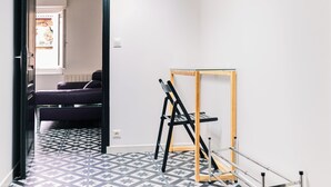 Een smalle gang met een vloer met een geometrisch patroon, een bed op de achtergrond en een ladder tegen de muur.