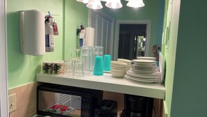 Una encimera de cocina con dispensador de toallas de papel, un microondas, una cafetera y varios vasos y platos.