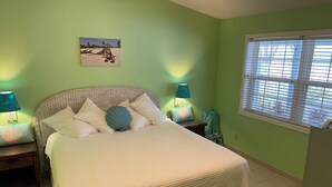 Un dormitorio con cama, dos mesitas de noche, una ventana con persianas y un cuadro colgado en la pared.