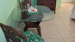 Un comedor con una mesa de vidrio, sillas de madera, un televisor en un estante y un armario.