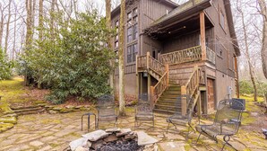 A rustic wooden cabin with a stone fire pit and metal chairs.
