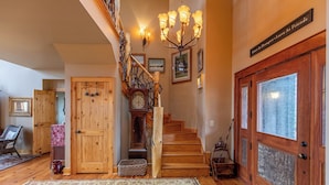 A wooden staircase with a chandelier, a large wooden door with frosted glass panels, and a rug on the floor.