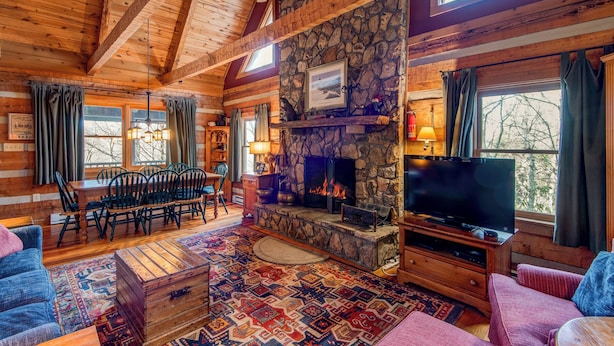 A cozy log cabin interior with a stone fireplace, wooden furniture, and a television. - Scarborough Fair (Banner Elk)