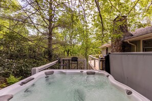 A hot tub surrounded by lush greenery and a wooden deck. - Bigfoot Bungalow (Blowing Rock)