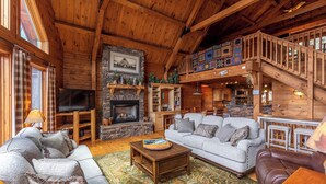 Interior espacioso de una cabaña de madera con chimenea, televisor y un rincón de estar acogedor.