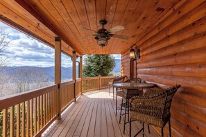 A wooden deck with a table and chairs, a ceiling fan, and a view of mountains. - Beary Relaxing Cabin (Banner Elk)