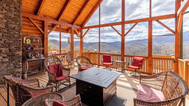 Terraza de madera con mobiliario de mimbre y un muro de piedra, con vistas a un paisaje montañoso.
